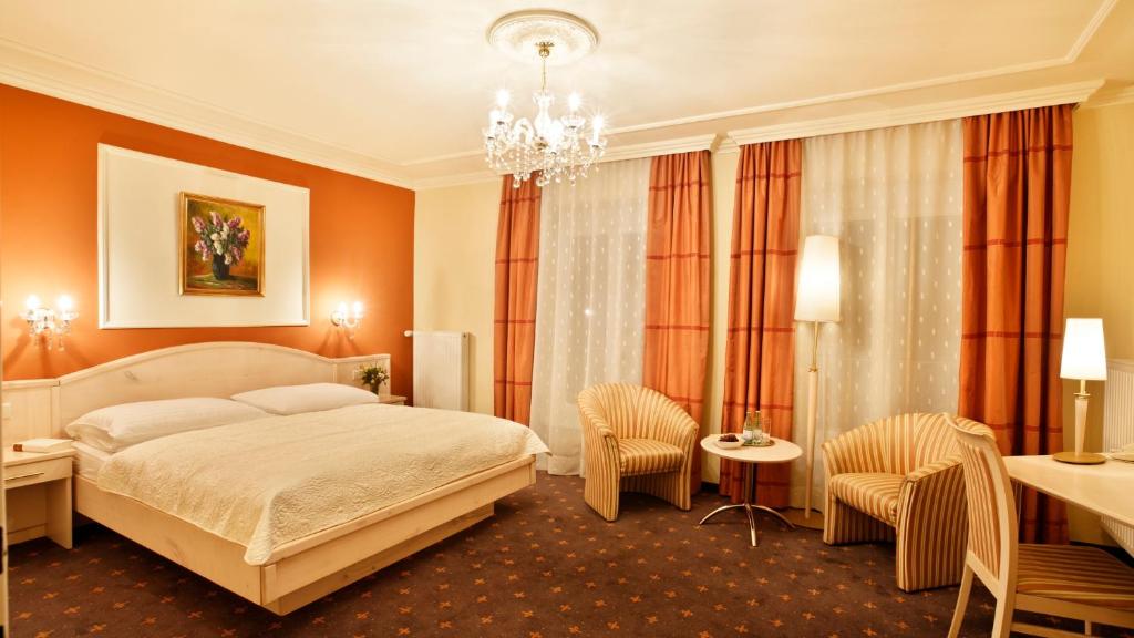 a bedroom with a bed and chairs and a chandelier at Hotel Stenitzer in Bad Gleichenberg
