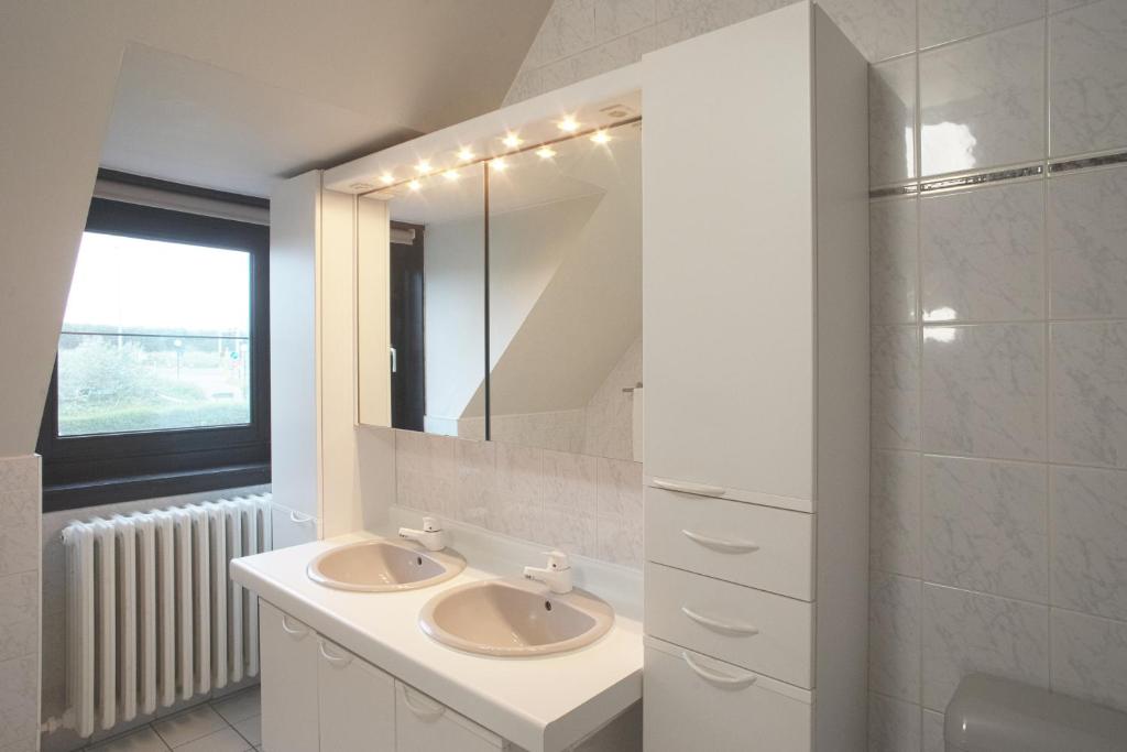 a white bathroom with two sinks and a mirror at Corsendonk Duinse Polders in Blankenberge
