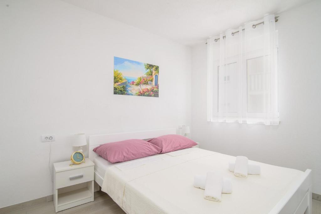 biała sypialnia z łóżkiem i oknem w obiekcie Apartmani Manuela w Okrugu Gornjim