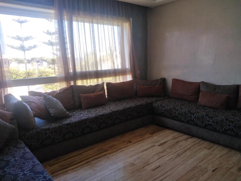 un sofá en una sala de estar con una gran ventana en Bel Appartement à PUERTO MARINA-DAR BOUAZZA avec piscines et jardins, en Casablanca