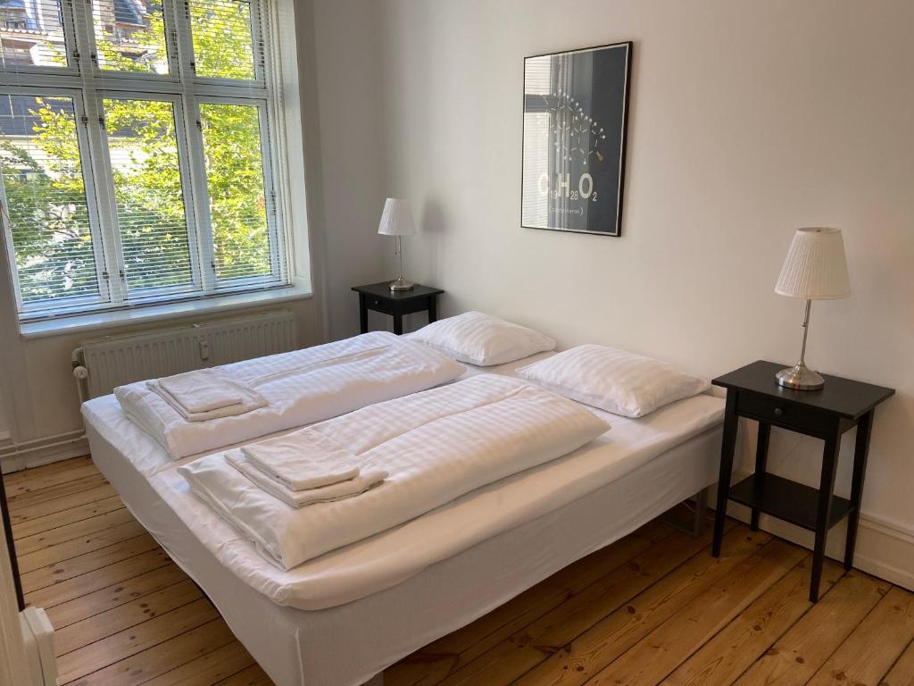 a white bed in a room with two tables and two windows at Koldinggade in Copenhagen