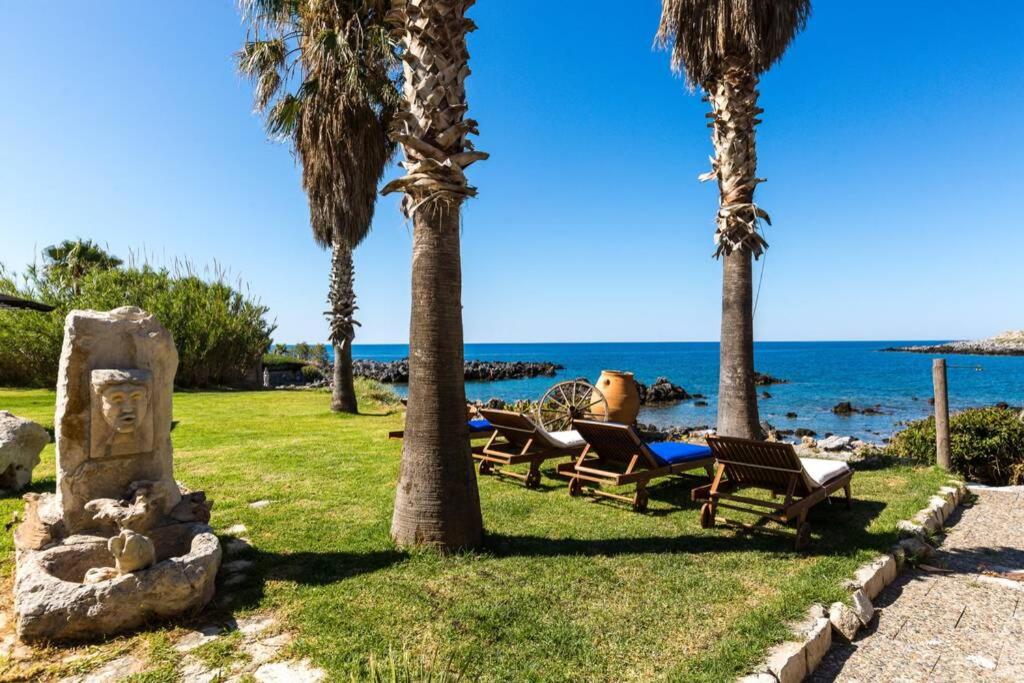 a park with palm trees and chairs and the ocean at Villa Proto Helidoni - A cozy beachfront Villa in Petres