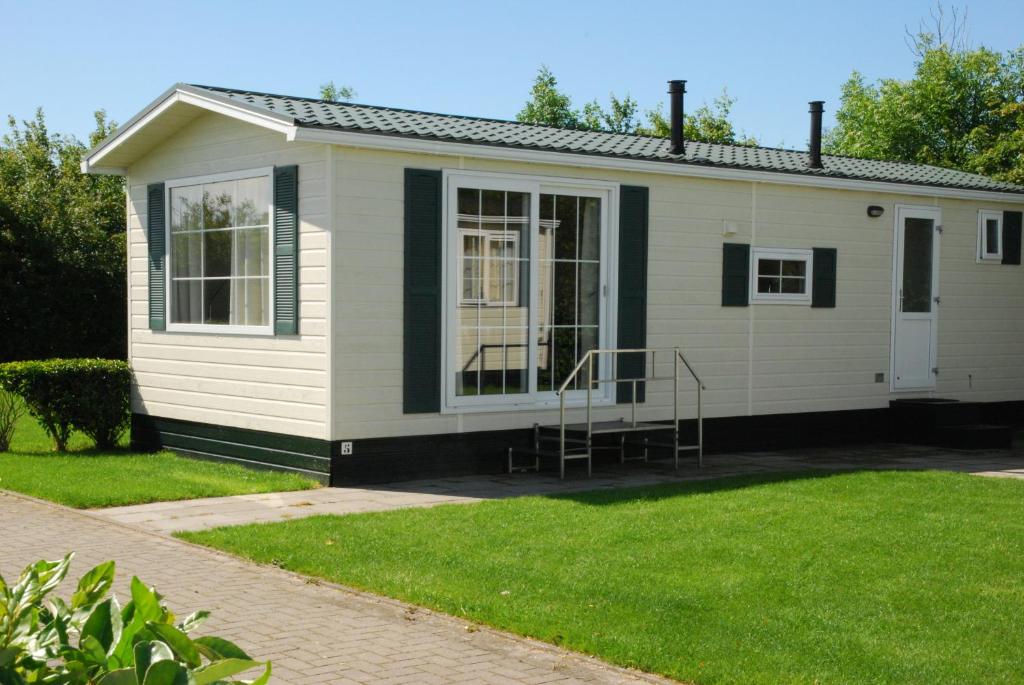 una pequeña casa blanca con césped delante en Minicamping De Visser, en Zoutelande