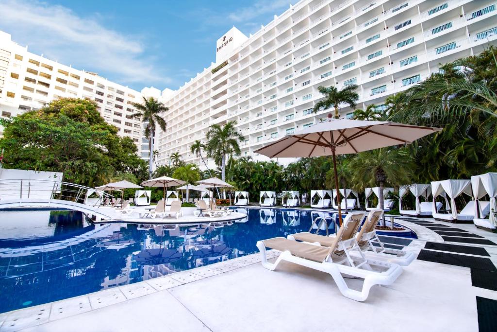 a hotel swimming pool with chairs and an umbrella at Emporio Acapulco in Acapulco