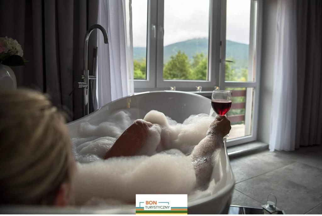 a woman laying in a bath tub with a glass of wine at FMA ski & bike in Szklarska Poręba