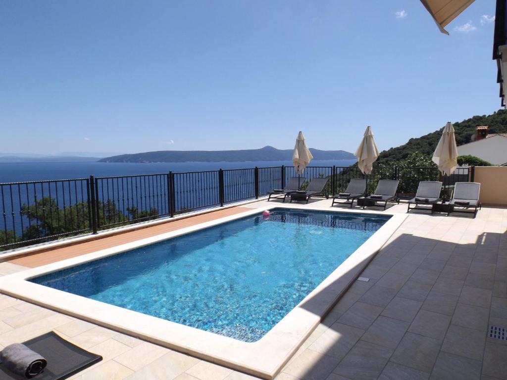 a swimming pool with chairs and a view of the ocean at Apartments Villa Elma in Mošćenička Draga