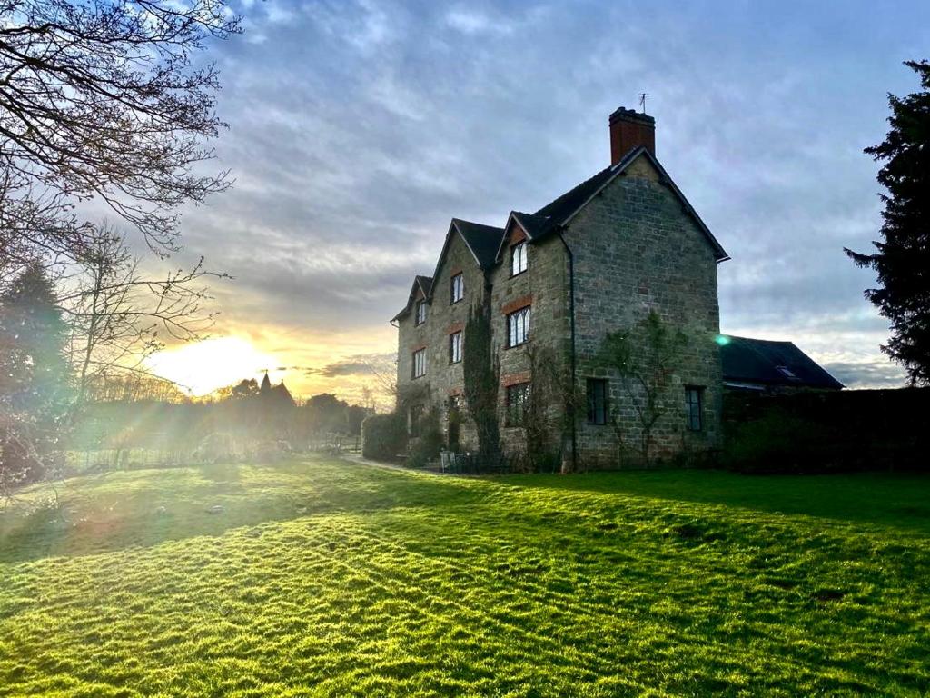 una casa vieja en un campo de hierba con la puesta de sol en el fondo en Abbey Farm Bed And Breakfast, en Atherstone