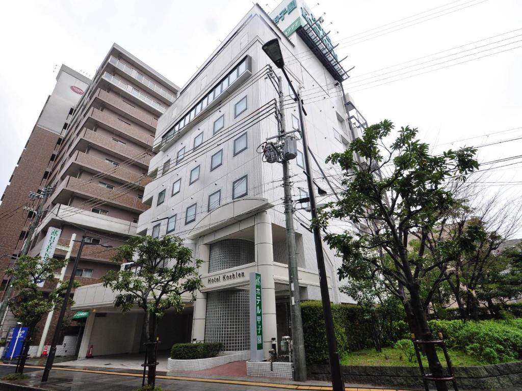 a large white building on a street with trees at Hotel Koshien in Nishinomiya
