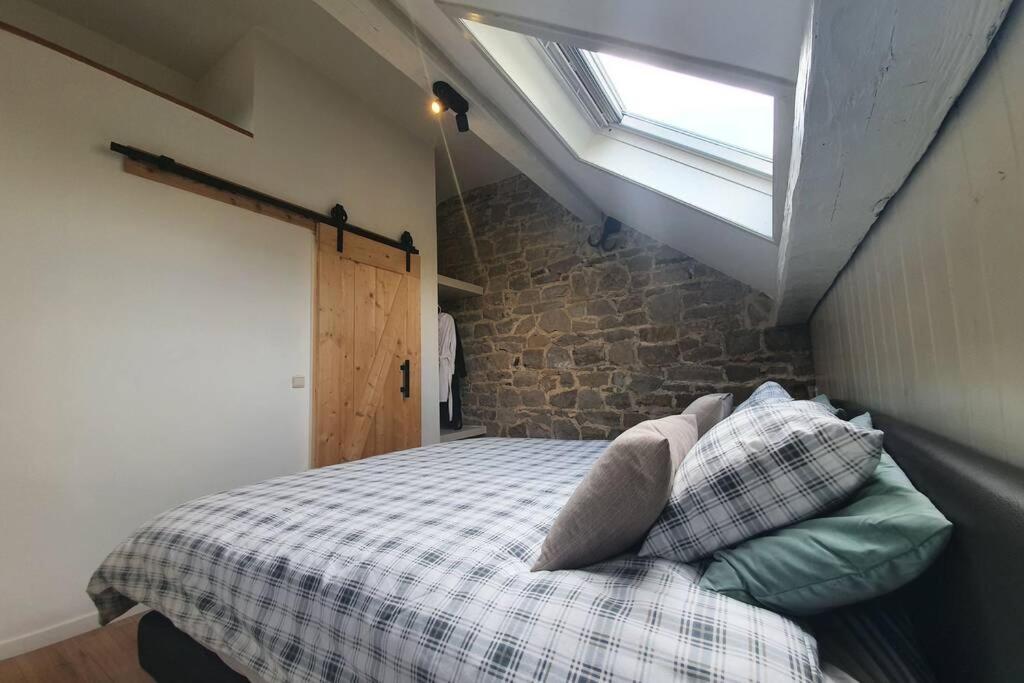 1 dormitorio con 1 cama con ventana y pared de ladrillo en Charmante duplex, en Andenne