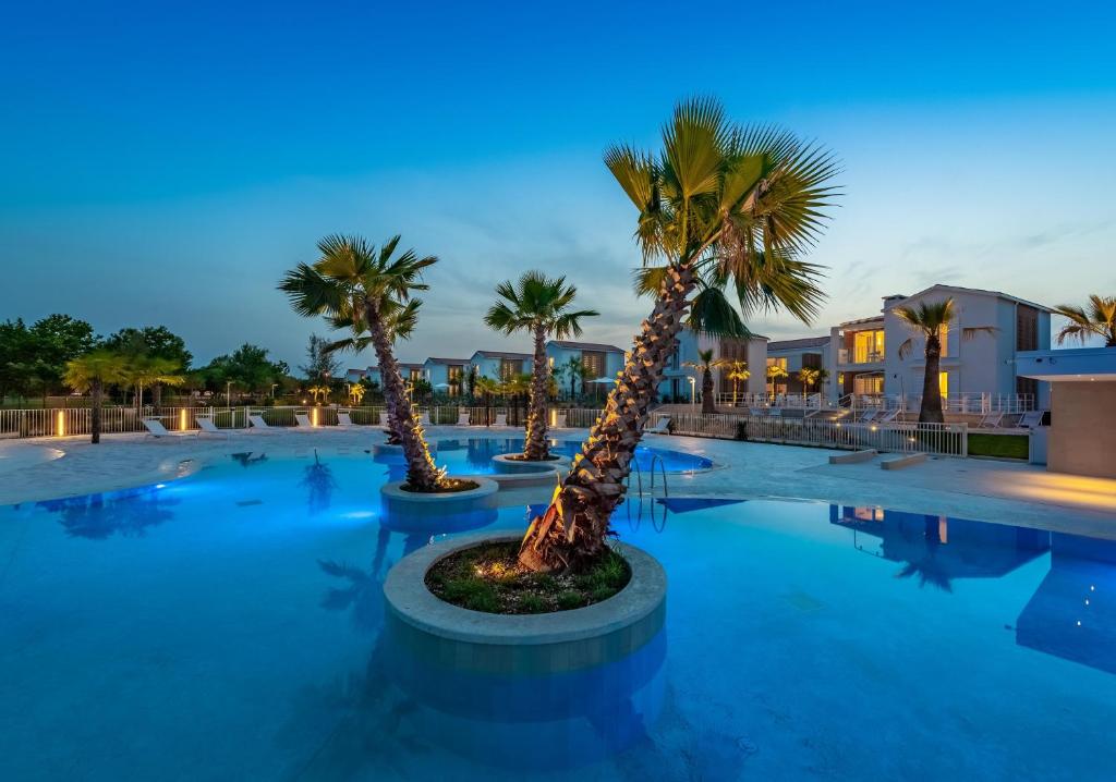 un grupo de palmeras en una piscina por la noche en Pareus Beach Resort en Caorle