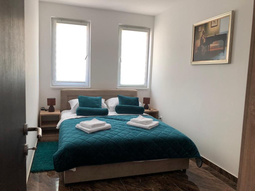 a bedroom with a bed with green sheets and two windows at Apartman Pino in Veliko Gradište