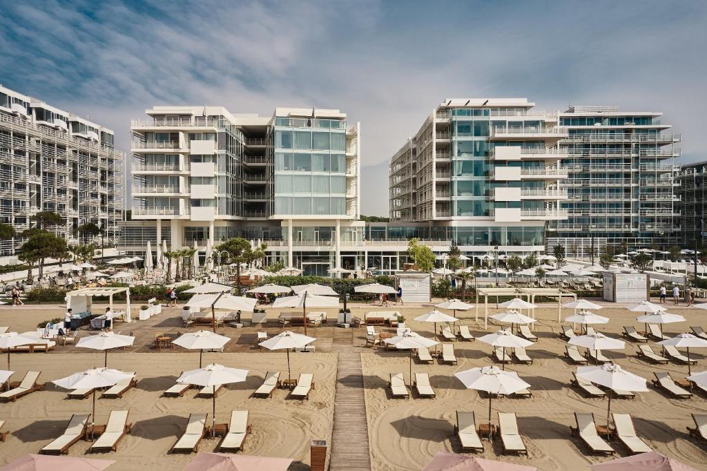 a beach with chairs and umbrellas in front of buildings at Falkensteiner Hotel & Spa Jesolo in Lido di Jesolo