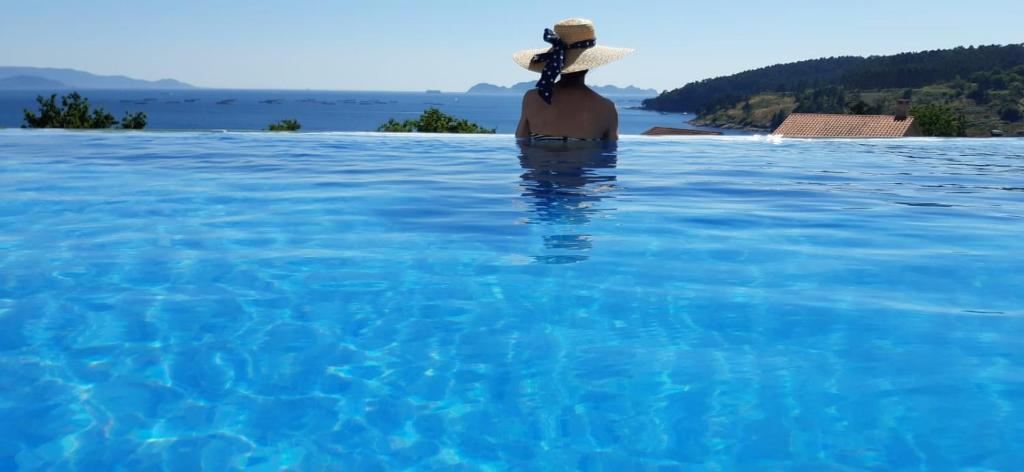 a woman in a hat sitting in a swimming pool at Chalet Mirador da Pinela in Cangas de Morrazo