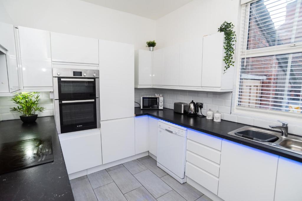 a kitchen with white cabinets and a black counter top at South Cheshire House in Wistaston