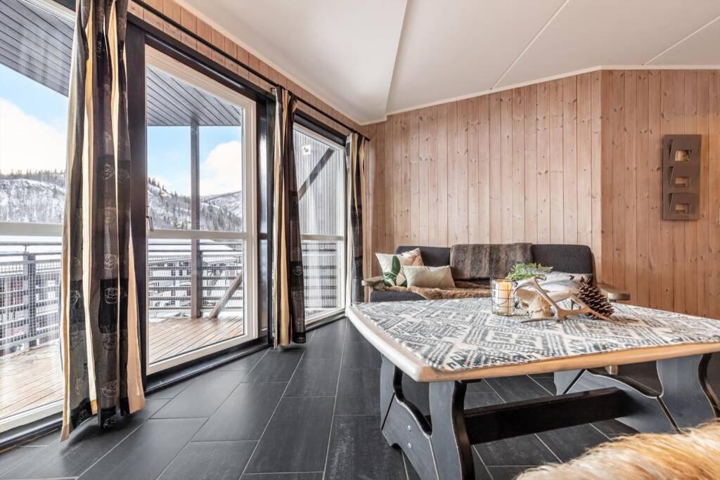 a living room with a table and large windows at Hemsedal-leilighet med 3 soverom, 2 bad og badstue in Hemsedal