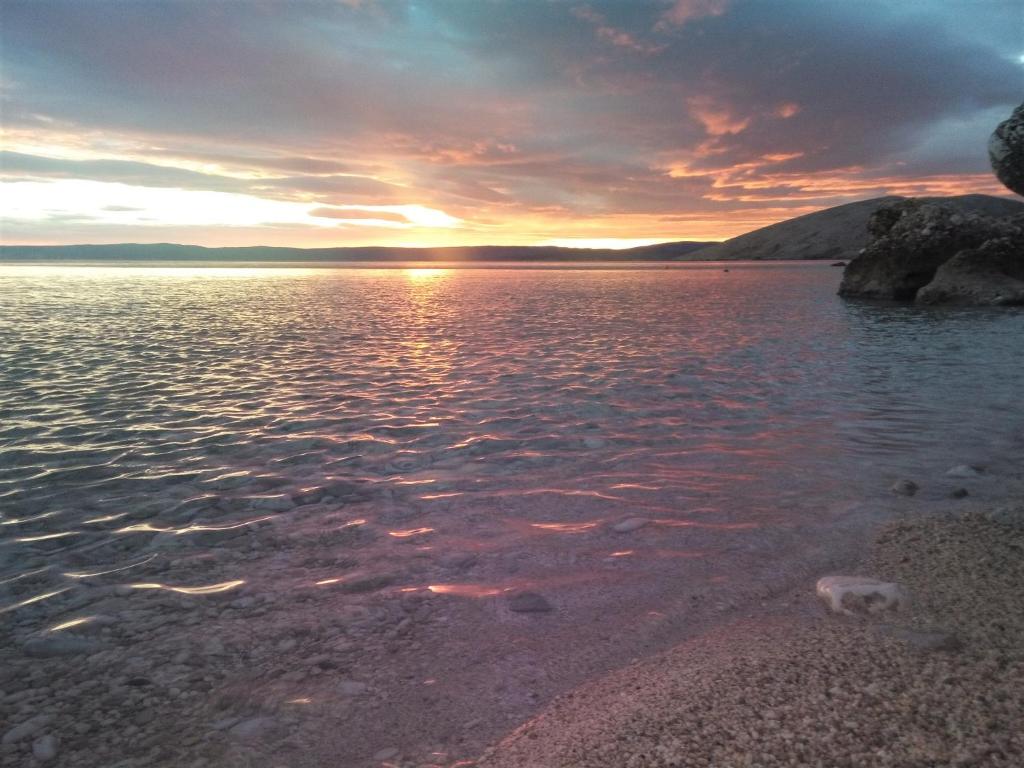 un tramonto su un corpo d'acqua con rocce di Agave apartments a Stara Baška