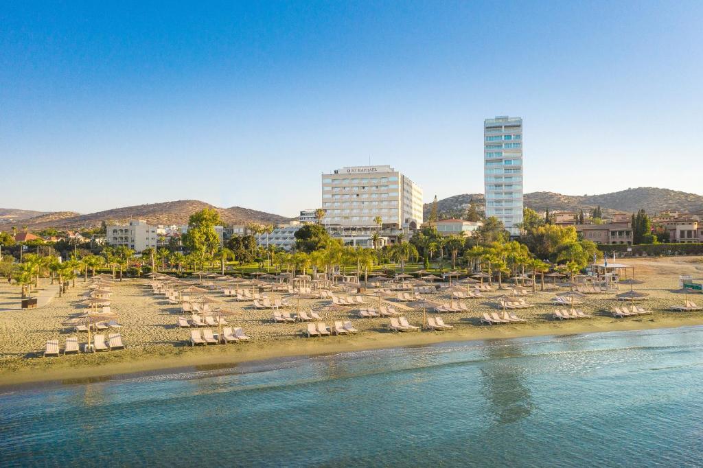 a beach with chairs and umbrellas next to the water at St Raphael Resort in Limassol