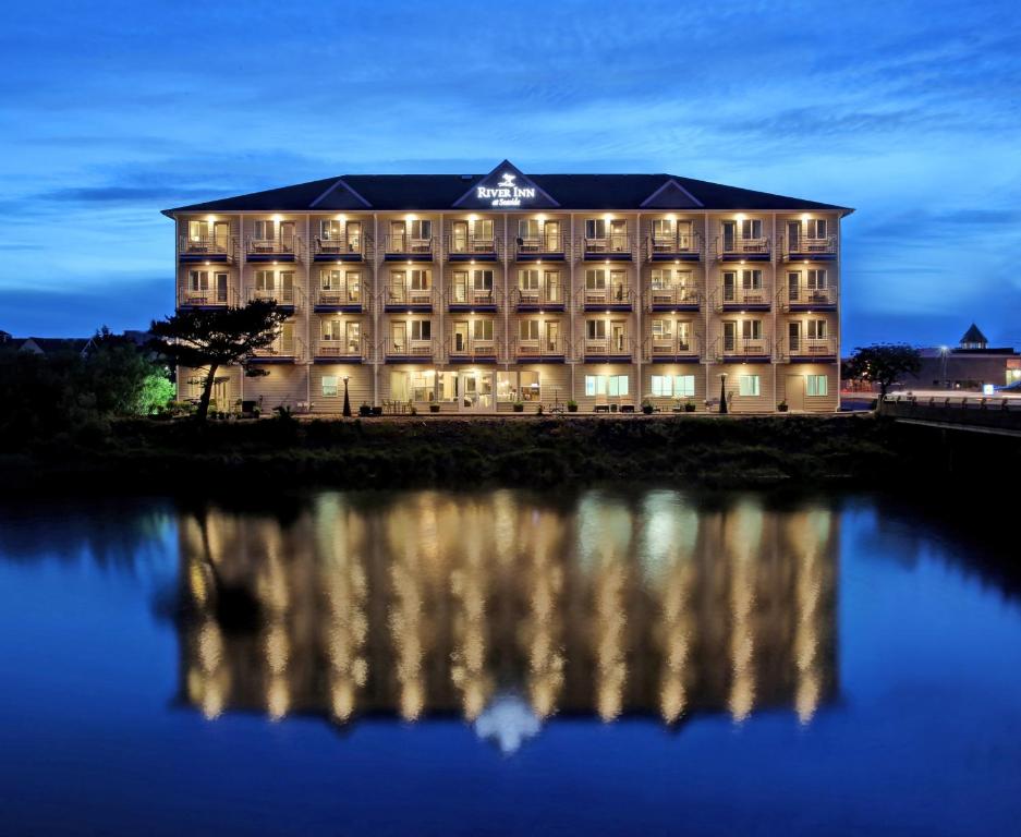 a hotel at night with its reflection in the water at River Inn at Seaside in Seaside