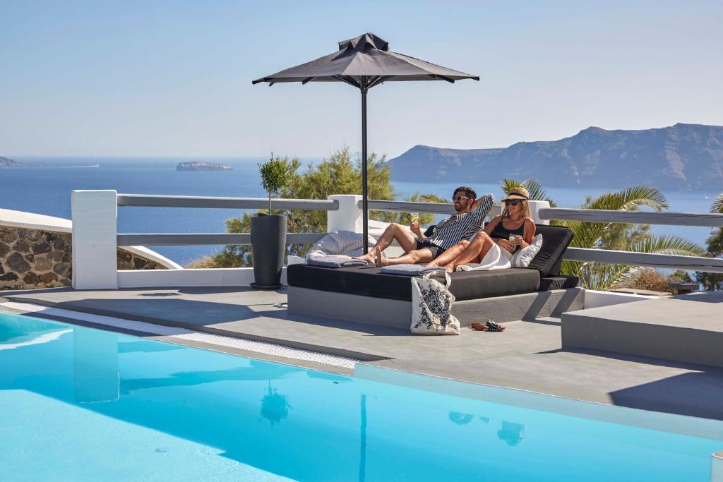 two people sitting on a couch next to a swimming pool at Mr and Mrs White Oia - Santorini in Oia