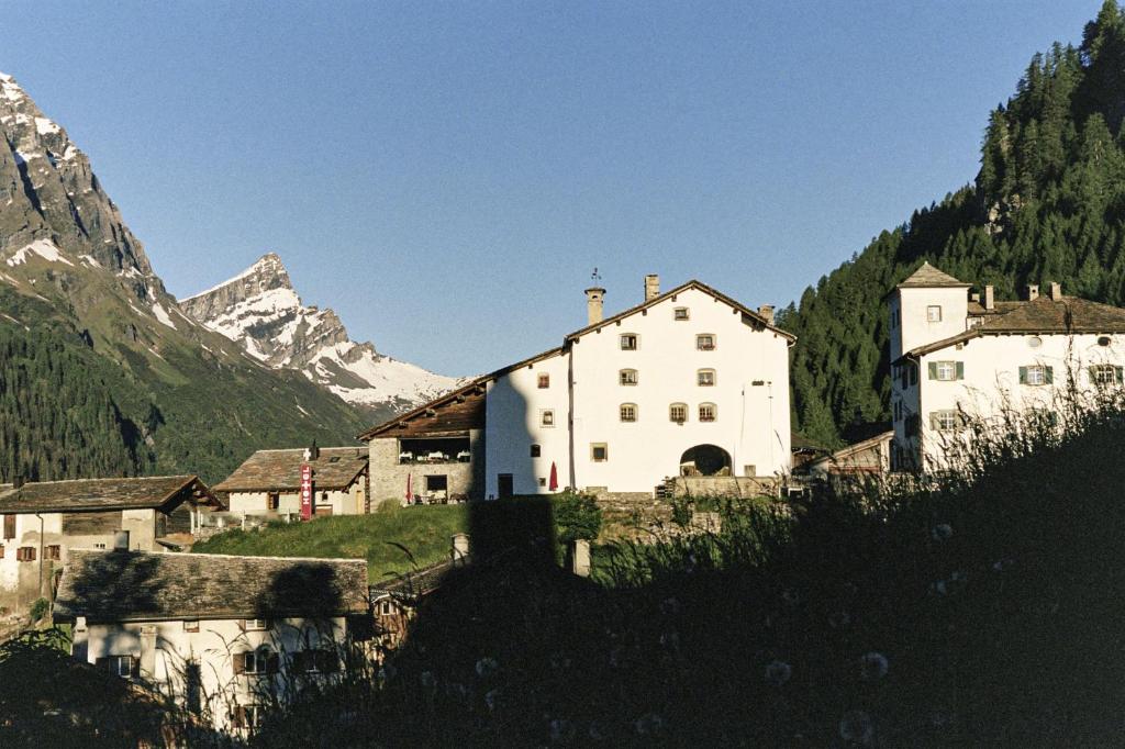 un groupe de bâtiments sur une colline avec une montagne dans l'établissement Hotel Weiss Kreuz, à Splügen