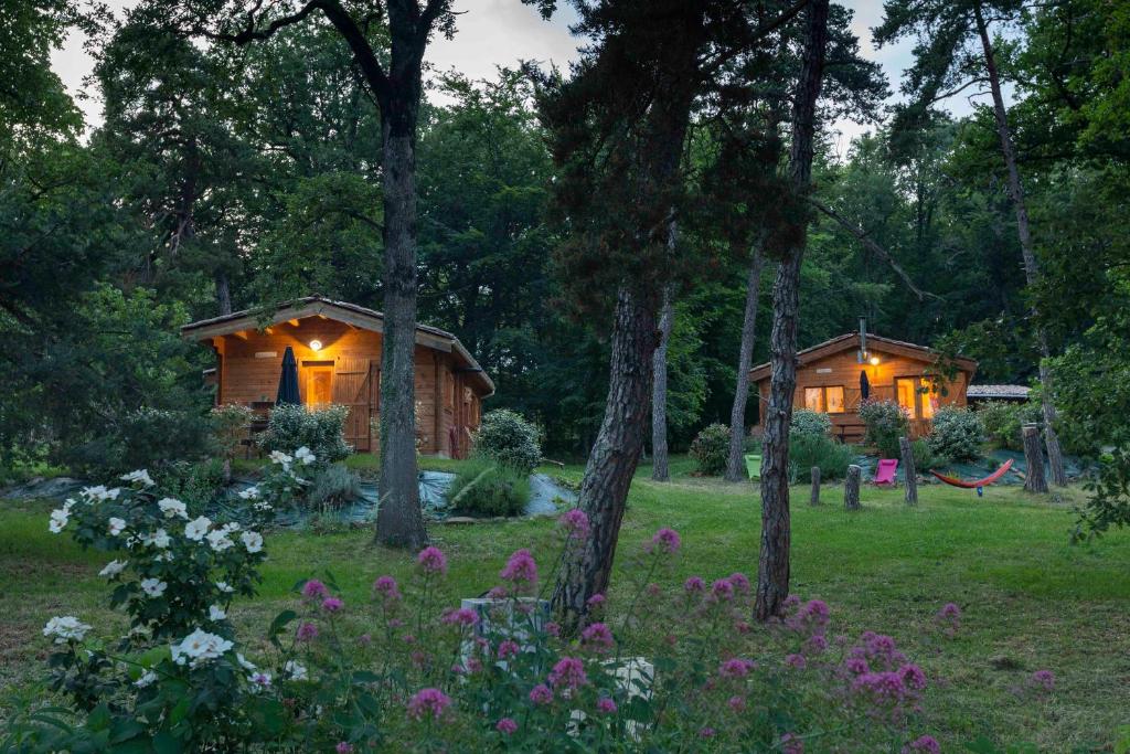 Chalets du Bois de Vache في Le Poët-Célard: كابينة في الغابة بها زهور وأشجار