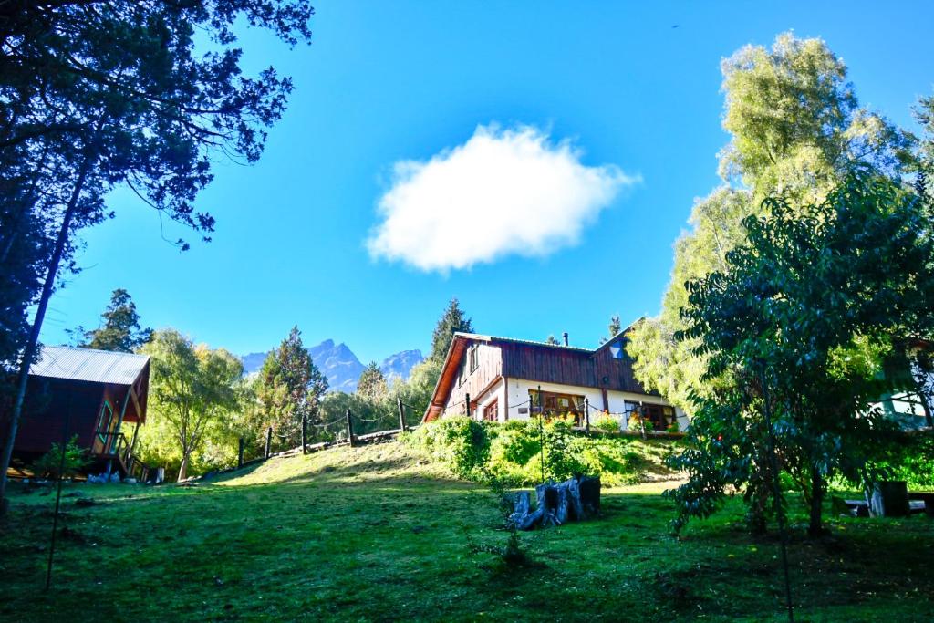 a house on a grassy field next to a building at Hostel El Mirador in El Bolsón