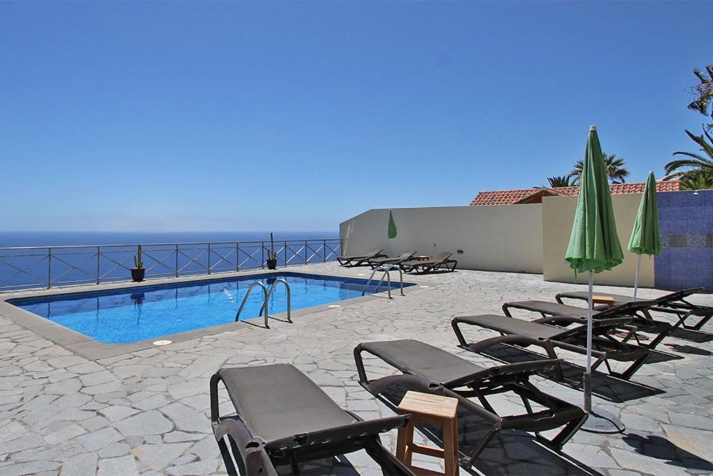 a group of chairs and umbrellas next to a swimming pool at Bungalow Moijama el Drago in Los Llanos de Aridane