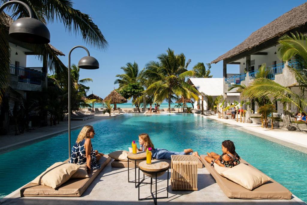 three girls sitting on lounge chairs by a swimming pool at Casa Beach Hotel "Casa Del Mar" in Jambiani