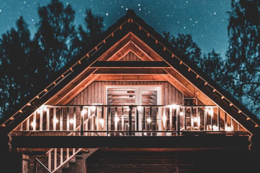 a log cabin with lights on the balcony at night at Hubane ja ruumikas katusealune majutus karjamõisa ajaloolises hoones in Plaani