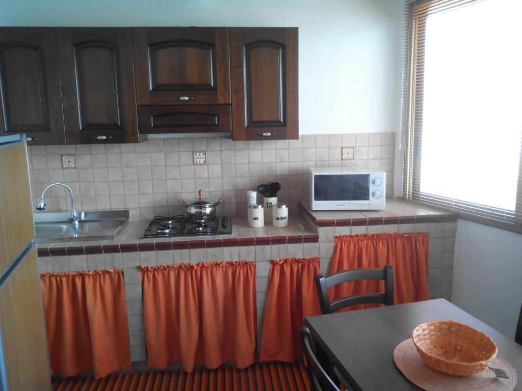 cocina con cortinas de color naranja, fogones y mesa en Casa Vacanza Za' Giuvannina, en Sciacca