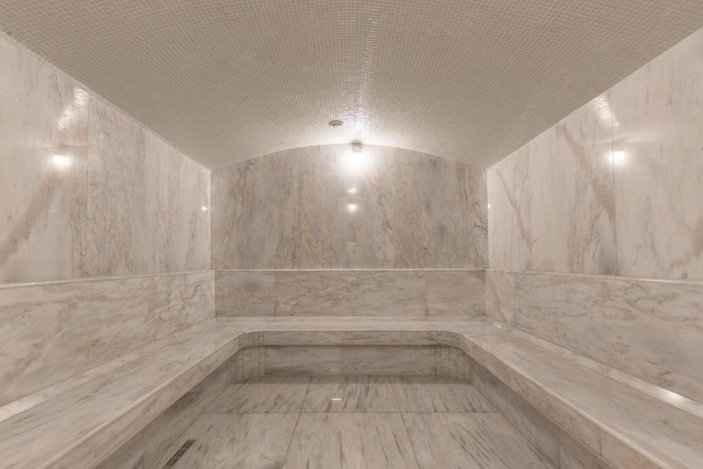 a room with a tub with marble walls and lights at Premium Park Hotel in Prizren