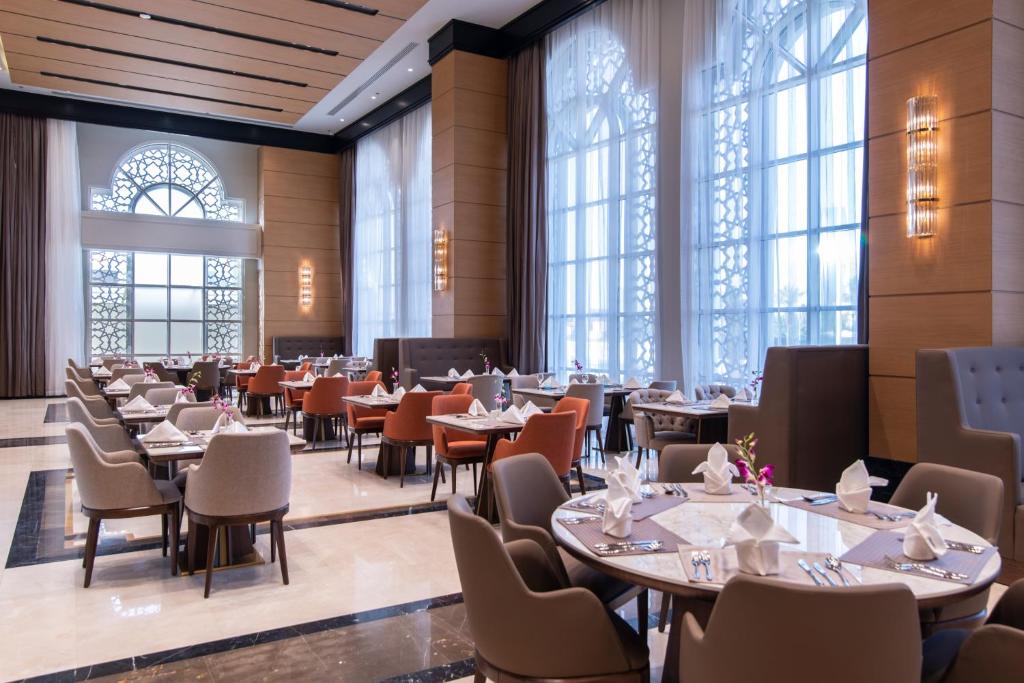 a dining room with tables and chairs and windows at Gardino Hotel & Residence in Riyadh