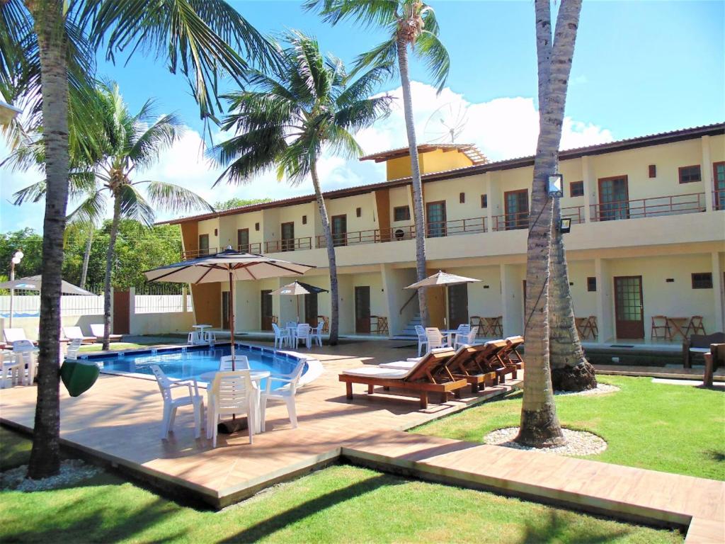 a resort with a pool and chairs and palm trees at Pousada Paraiso da Barra in Barra de Santo Antônio