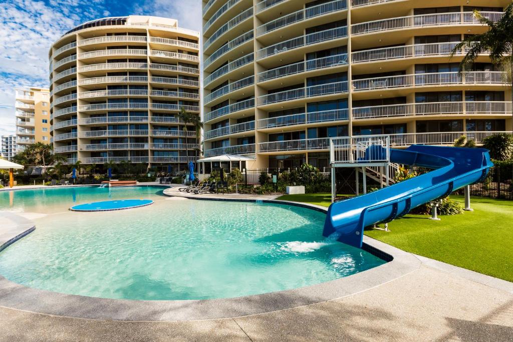 a large swimming pool with a blue slide in front of a building at Gemini Resort in Caloundra