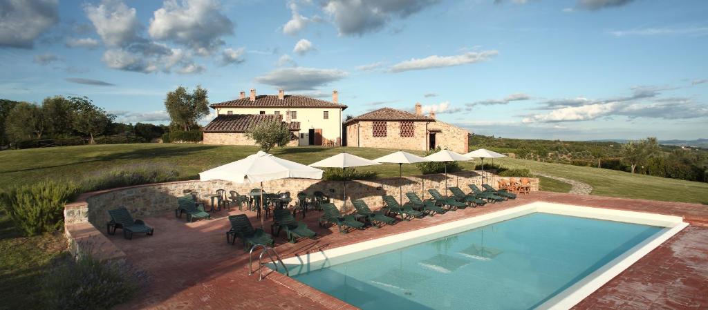 a swimming pool with chairs and umbrellas in front of a house at Agriturismo Podere Fornacino in Castelnuovo Berardenga