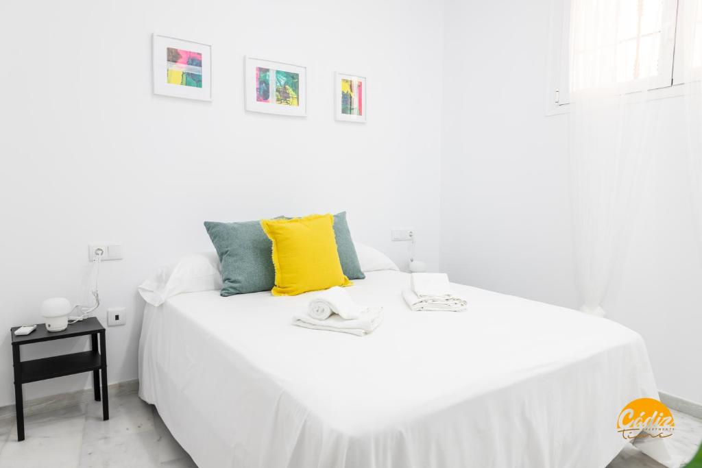 a white bed with a yellow pillow on top of it at Casa Patio La Viña by Cadiz Time in Cádiz