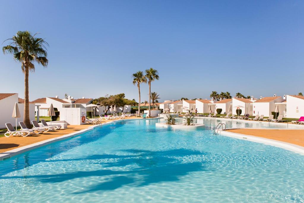 a large swimming pool with palm trees and houses at Sagitario Menorca Mar Adults only in Cala'n Bosch