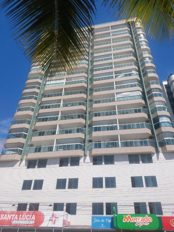 a tall white building with a palm tree in front of it at Frente Mar Green Diamond Residencial in Vila Velha