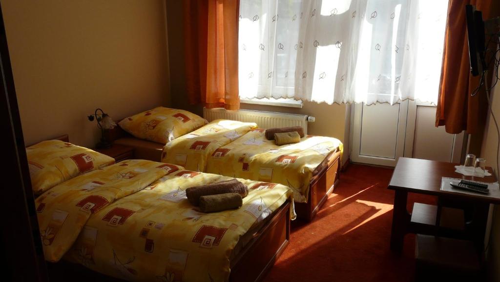 a room with two beds and a table and windows at Hotelik Parkowy in Legnica