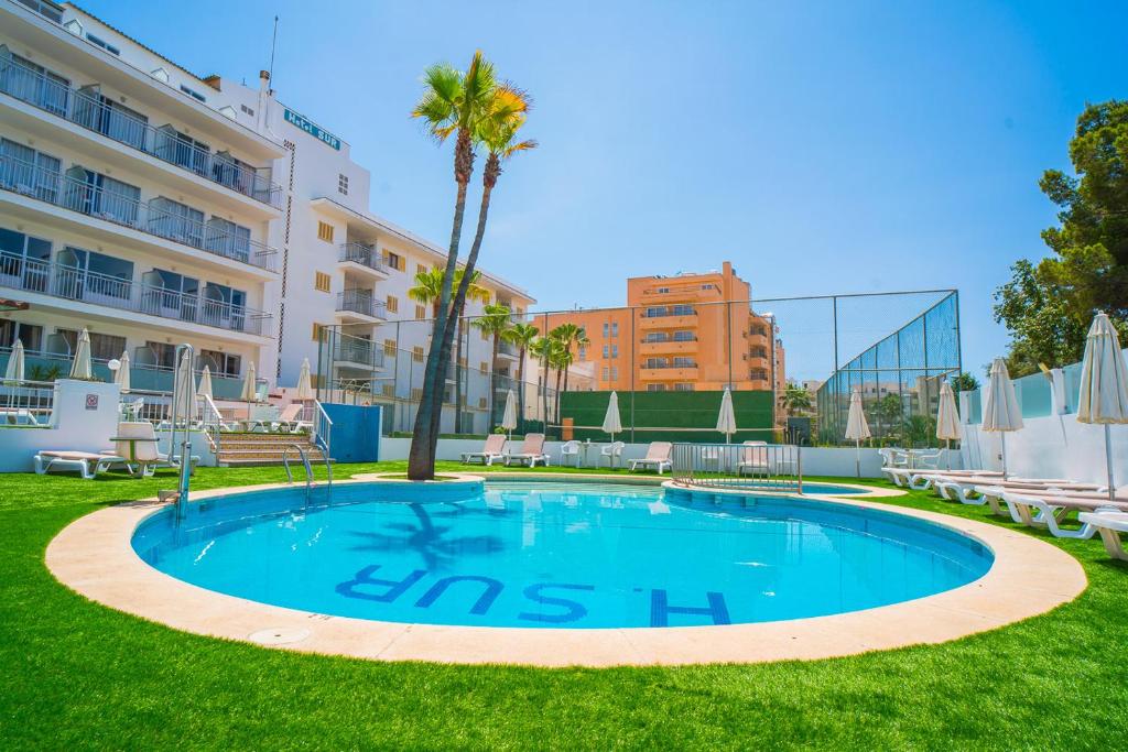 una piscina en medio de un césped con palmeras y edificios en Hotel Sur, en Cala Bona