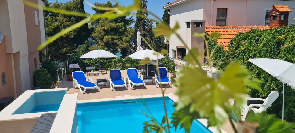 a pool with blue chairs and umbrellas next to a building at Apartments Villa Natali - Heating Pool in Trogir
