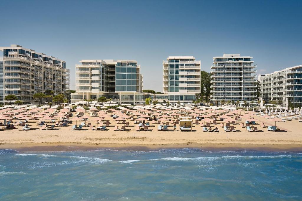 a beach with chairs and umbrellas and tall buildings at Falkensteiner Residences Jesolo in Lido di Jesolo