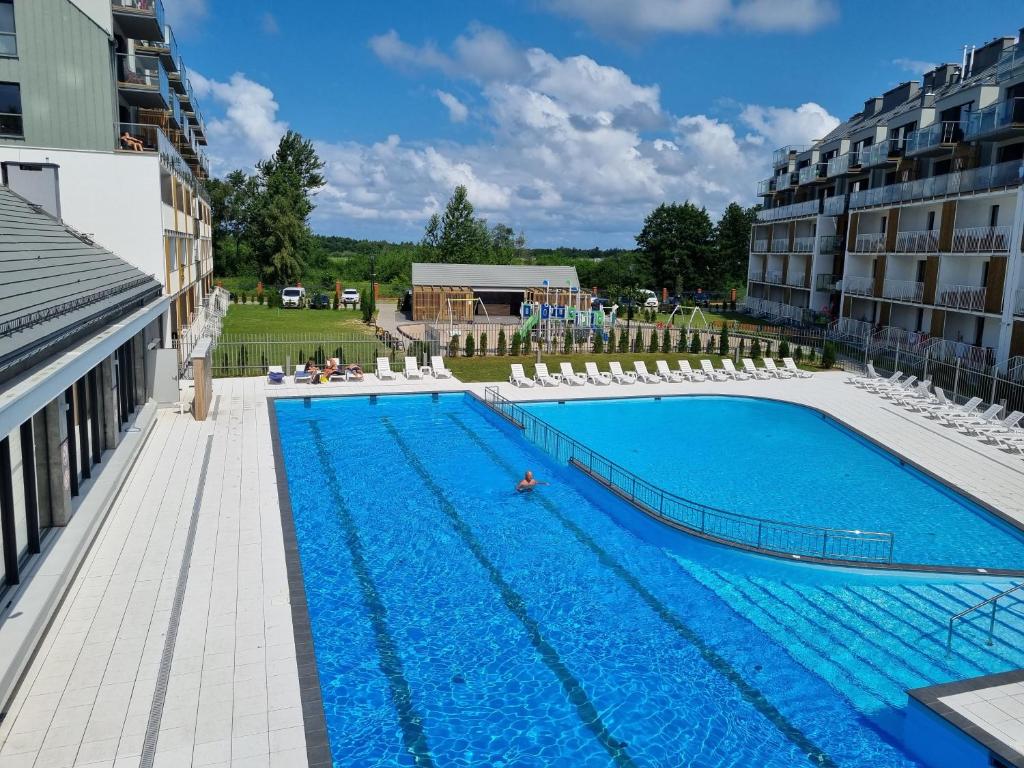 uma grande piscina com cadeiras brancas e um edifício em Apartament z widokiem, osiedle FENIKS em Kolobrzeg