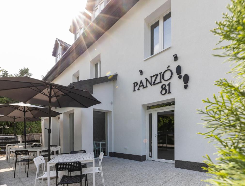a white building with tables and umbrellas in front of it at Panzió 81 in Hajdúszoboszló