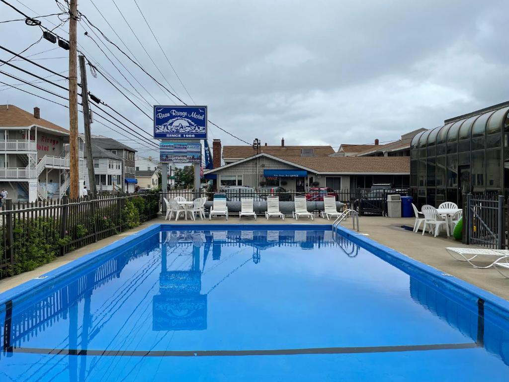a large blue swimming pool with chairs and tables at Beau Rivage Motel in Old Orchard Beach