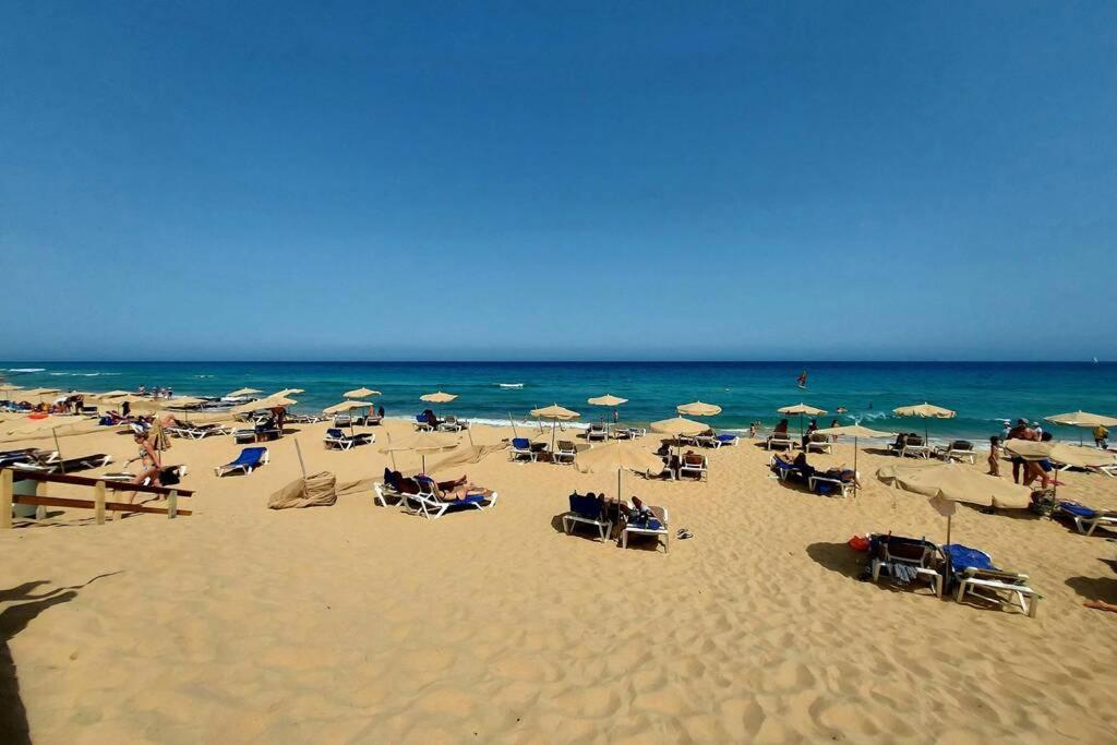 uma praia com muitas cadeiras e guarda-sóis e o oceano em Amplio apartamento en la playa del Esquinzo em Playa Jandia