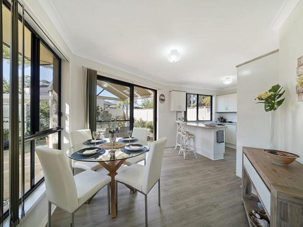 a dining room with a table and white chairs at Escape to Janeli by Experience Jervis Bay in Vincentia