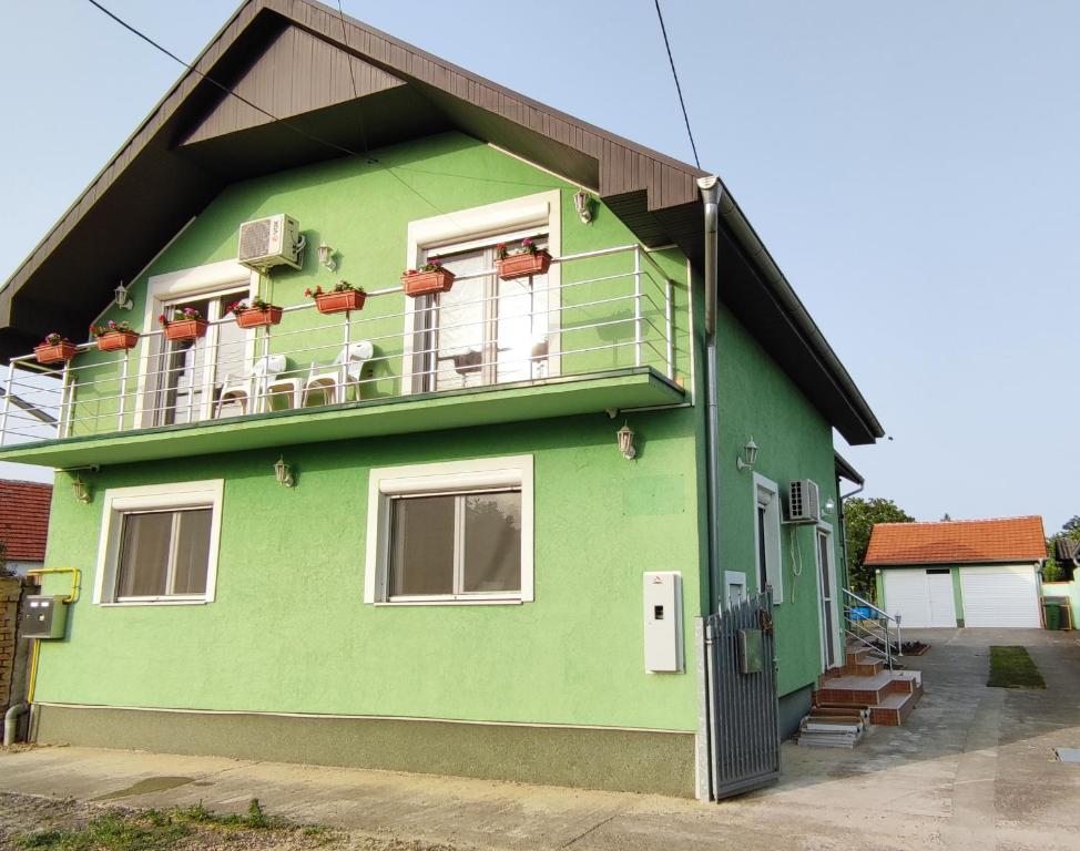 ein grünes Haus mit einem Balkon mit Stühlen darauf in der Unterkunft Guest House Jovanovic in Melenci