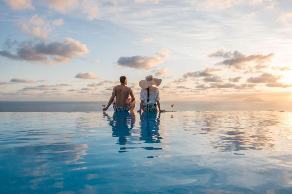 dois homens sentados na piscina de beiral infinito de um resort em Hotel Ravesi em Malfa
