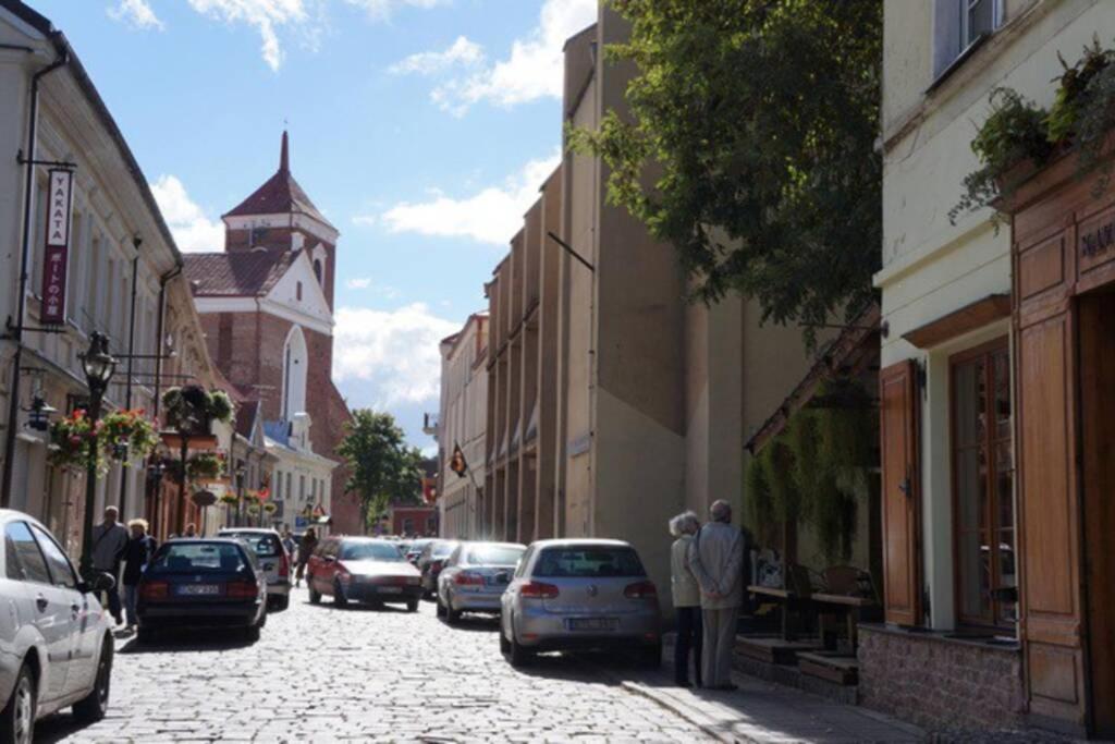 a street with cars parked on a cobblestone street with a clock tower at In the heart of Kaunas in Kaunas